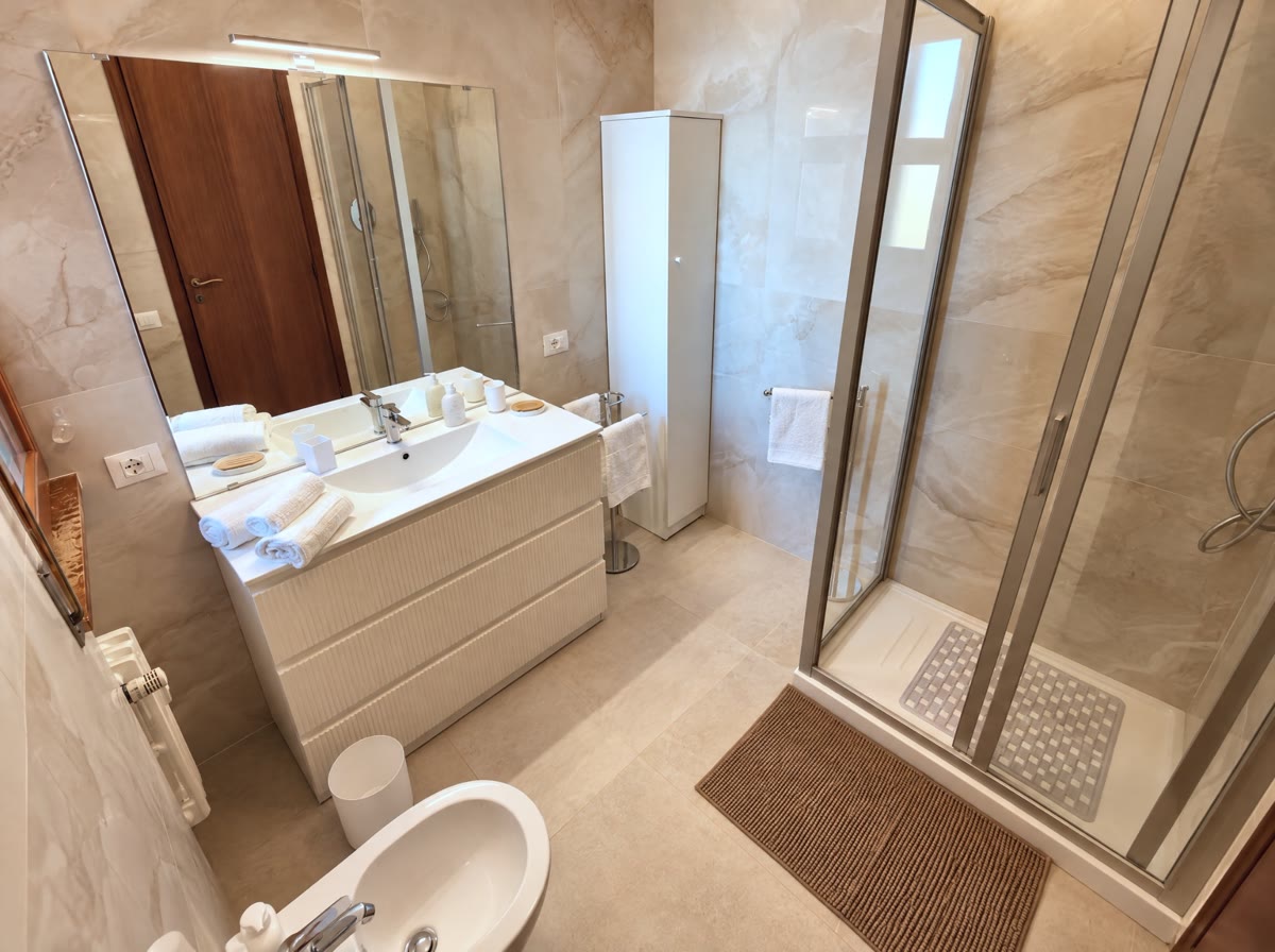 Bagno in marmo chiaro con mobile bianco e box doccia