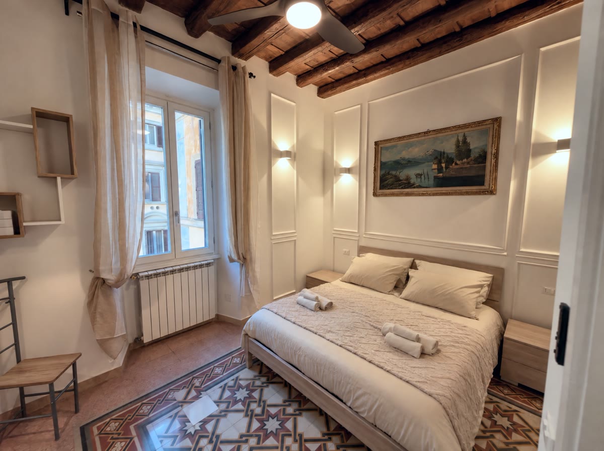 Camera con soffitto a travi, pavimento in cementine e finestra sui palazzi del centro